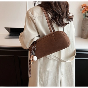 Brown frosted suede baguette bag with baseball charm shown on shoulder over a beige coat