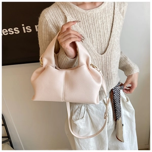 Detail view of pink textured leather crossbody bag with pleated sides and gold hardware