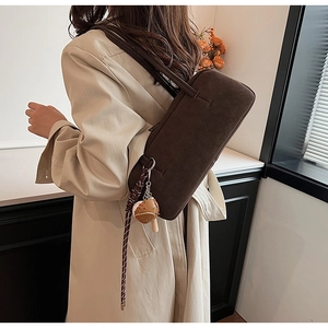 Detail of dark brown suede baguette bag with a mini croissant charm on a trench coat
