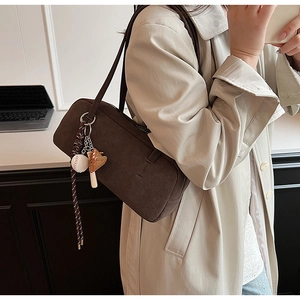 Detailaufnahme einer dunkelbraunen Wildleder-Schultertasche mit Baseball-Anhänger