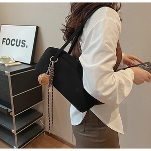 Detail einer schwarzen Canvas-Schultertasche mit Plüsch-Anhänger an einem Modell