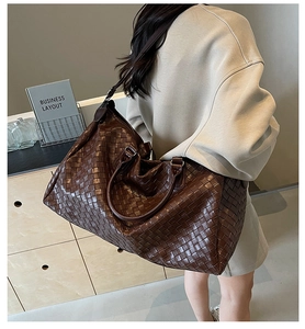 Large dark brown woven leather travel duffle bag carried over shoulder by a woman