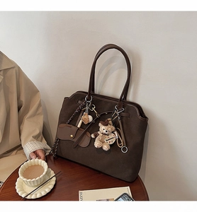 Detail of dark brown suede tote bag with plush charm and metal chain on wooden table