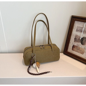 Detail der olivgrünen Wildleder-Baguette-Tasche mit Baseball-Anhänger und Doppelgriffen