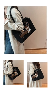 Detail of a large black suede tote bag with plush bear charm and glasses case accessory