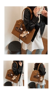 Detail of a large brown suede tote bag featuring a plush bear and mini leather charms