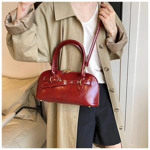 Detailansicht der glänzenden roten Ledertasche mit elegantem Gürtel und goldener Hardware.