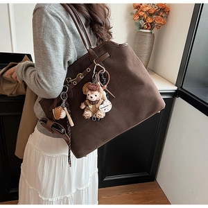 Detail of dark brown faux suede tote bag featuring plush charms and long shoulder straps