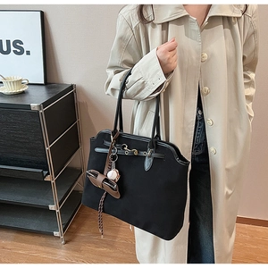 Detail of black suede tote bag with metal buckle and decorative baseball charm
