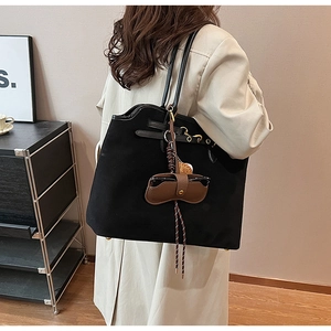 Model wearing a black matte suede tote bag with a unique brown leather glasses case charm