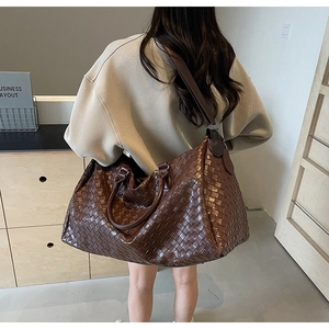 Model carrying a large dark brown woven travel bag in a modern minimalist indoor setting