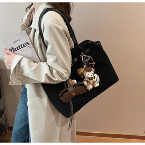 Close-up of a black suede tote bag featuring a decorative plush bear and mini leather charms