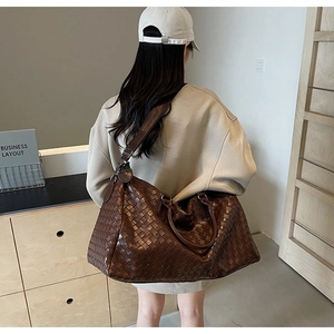 Macro view of the large brown woven travel bag shown on a model from the back
