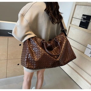 Large dark brown woven travel duffle bag with shoulder strap shown in use by a model