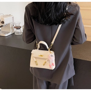 Detail of white embossed leather handbag featuring golden lock and pink plush charm accessory