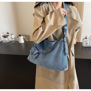Detail of light blue denim tote bag with metal chain and mini pouch on model shoulder