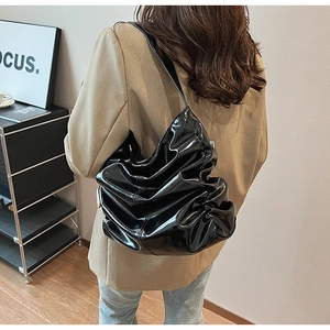 Dettaglio posteriore della borsa hobo nera lucida con pieghe indossata da modella