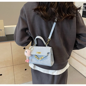 Detail of light blue embossed crossbody bag with gold hardware and pink plush charm