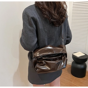 Detail of dark brown glossy patent leather pleated shoulder bag with sleek metal hooks