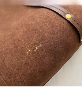 Close-up of brown suede tote bag featuring a decorative leather strap and gold round stud