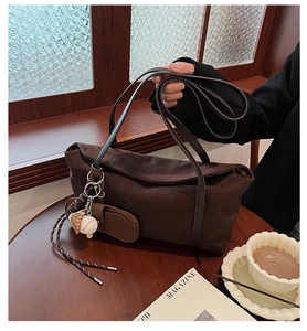 Detail of suede shoulder bag in dark coffee with baseball charm and matte texture