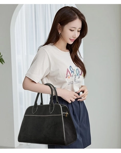 Close-up of black matte handbag featuring white contrast stitching and round handles