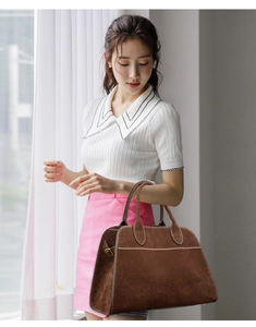 Detail of dark brown suede handbag featuring visible white stitching and leaf-shaped handle stitching