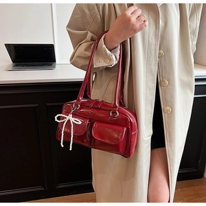 Detail of red patent leather shoulder bag with front pockets and pearl bow charm