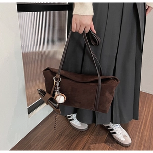 Detail of dark brown suede shoulder bag with minimalist baseball charm and small pouch