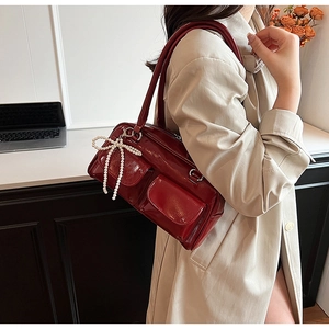 Gros plan d'un sac à bandoulière en cuir verni rouge vin avec breloque nœud en perles