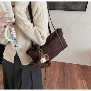 Détail du sac bandoulière en daim marron foncé avec petit charm et logo en cuir embossé