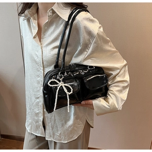 Detail of black patent leather bag with two front pockets and pearl bow charm accessory