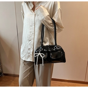 Détail du sac à bandoulière en cuir verni noir avec charm nœud papillon en perles