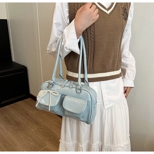 Detail of light blue glossy Boston bag featuring front pockets and pearl bow charm accessory