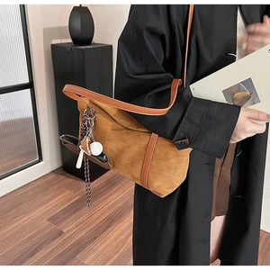 Detail of caramel suede shoulder bag with brown strap and baseball charm accessory