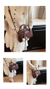 Detail of a brown leather shoulder bag featuring a unique baseball glove charm and zipper
