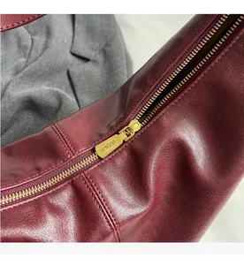 Detailed close-up of smooth gold metal zipper on a premium burgundy PU leather handbag