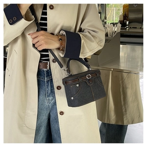 Detail of blue denim handbag featuring a pocket design, brown leather belt, and metal rivets