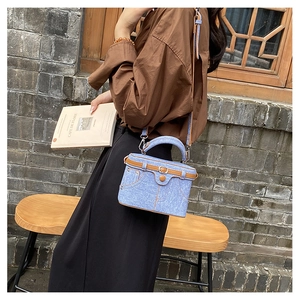 Detail of blue denim box bag featuring brown leather trim and retro pocket design