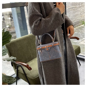 Detail of denim vanity case bag with brown trim and metal strap in home setting