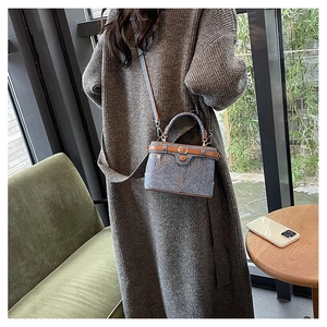 Blue denim box bag with brown leather trim shown on a model in a cozy indoor setting