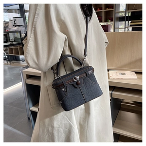 Detail of denim box bag with brown leather trim and metal clasp in a cafe setting