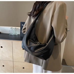 Minimalist black PU leather crescent shoulder bag shown in an elegant indoor lifestyle setting