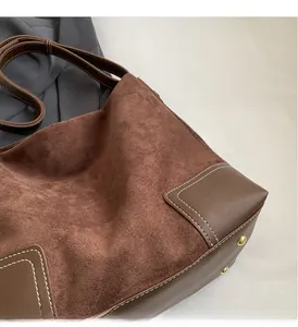 Detail of brown suede tote bag with white stitching and gold protective rivets