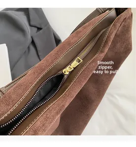 Detail of smooth gold zipper and white stitching on brown suede shoulder bag