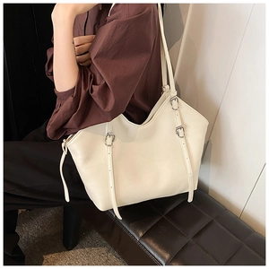Close-up of cream tote bag featuring adjustable buckle straps and leather texture