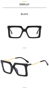Detailed close-up of large square black glasses frames with gold metal temples