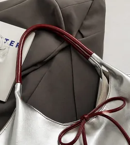 Detail of silver textured PU tote bag with red bow accent and glossy shoulder strap