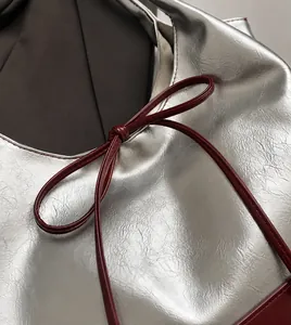 Detail of silver embossed faux leather bag with dark red bow-tie decorative cord