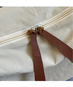 Detail of silver zipper pull with brown leather strap on beige nylon dumpling bag